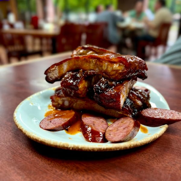 Luka's Barbecue ribs and sliced sausage on a plate, with a blurred restaurant background.