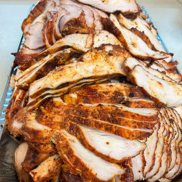 Close-up of a large catering tray filled with thinly sliced, seasoned barbecue chicken.