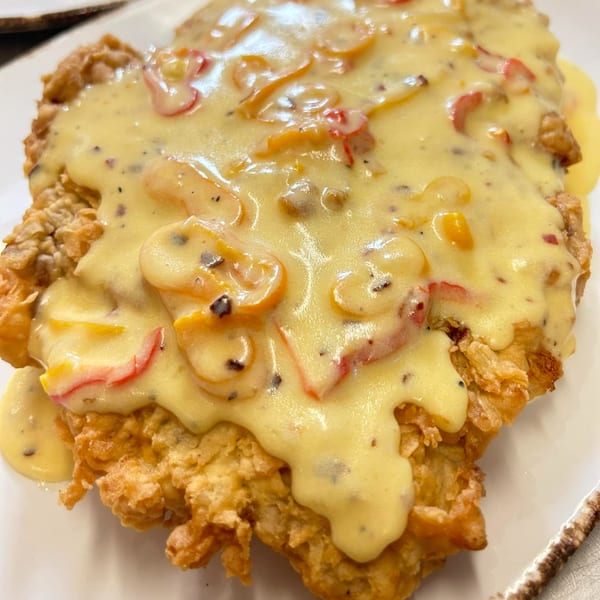 Crispy fried chicken steak smothered in creamy yellow sauce with red and yellow bell peppers.