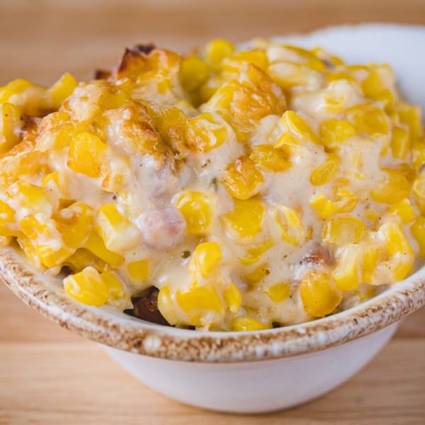 Creamy, cheesy corn casserole with golden-brown topping in a white bowl on a wooden table.