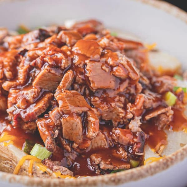 Close-up of a loaded baked potato with barbecue brisket, shredded cheese, and green onions.