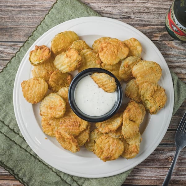 A white plate filled with golden-brown fried pickles and a small bowl of ranch dipping sauce.